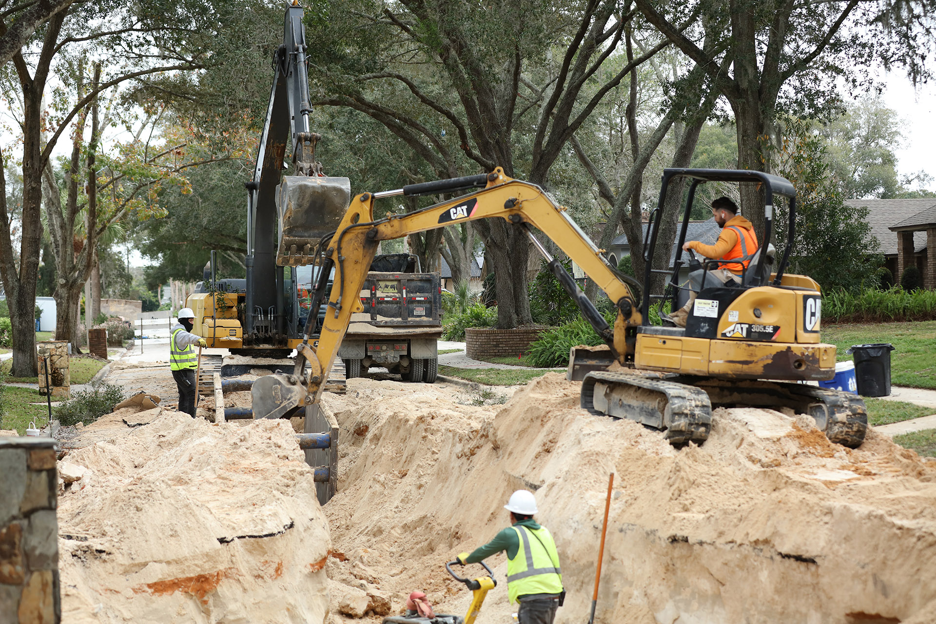 Excavator digging up sidewalk to get to pipes.